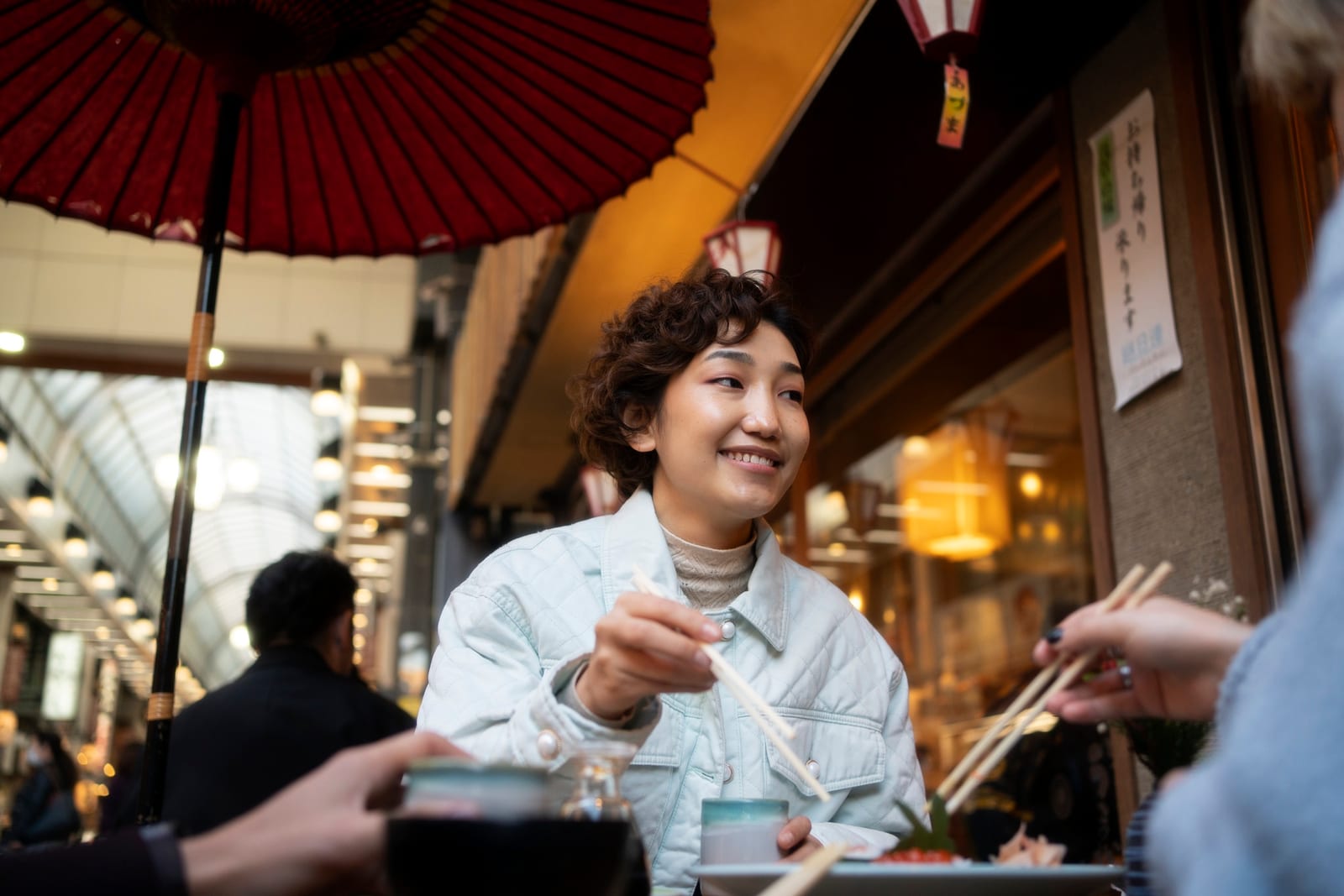 屋根付き市場の屋台で箸を使って食事をする日本人女性