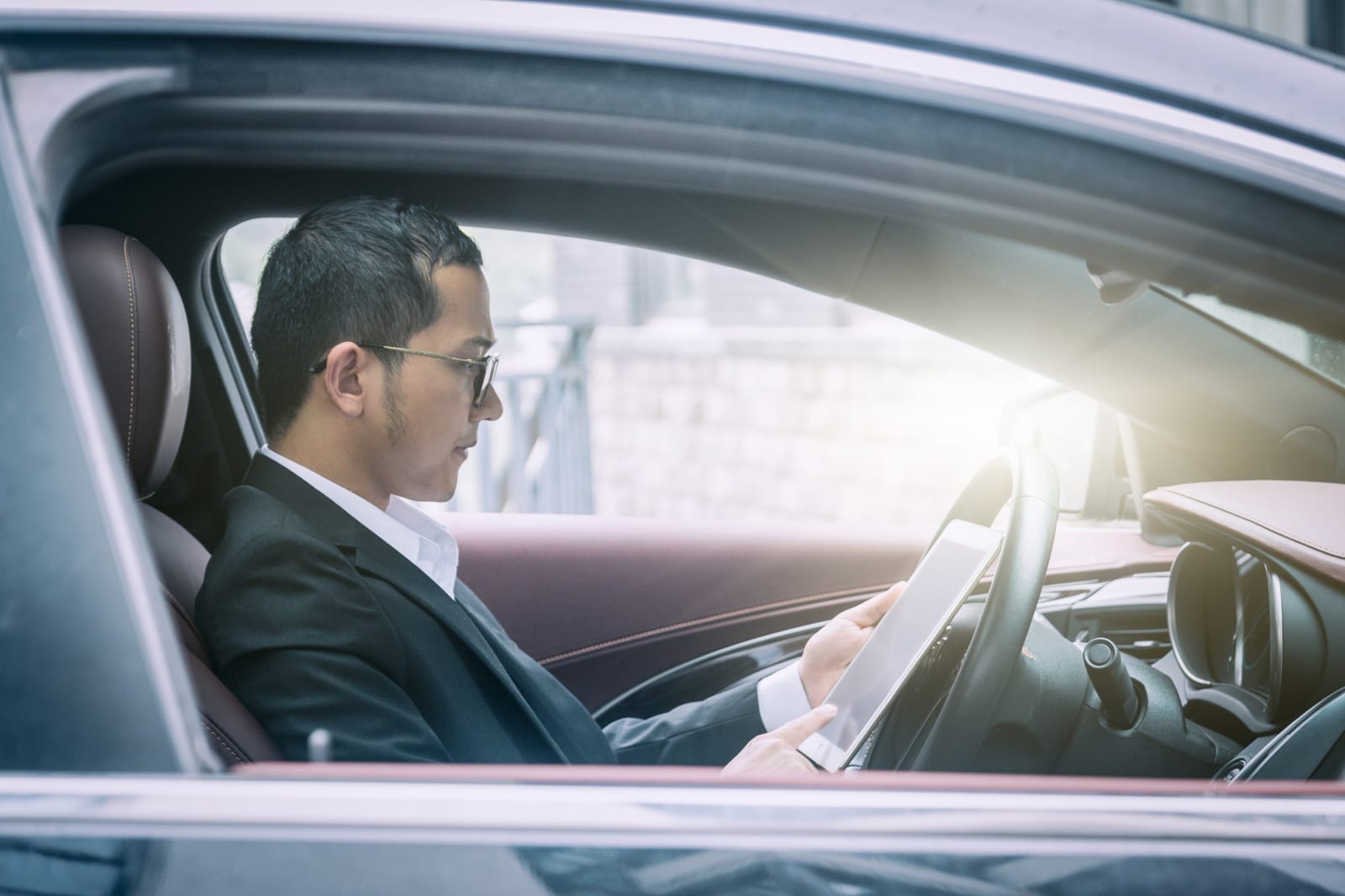バーガンディ色の革内装の車内でタブレットを確認するスーツ姿の男性